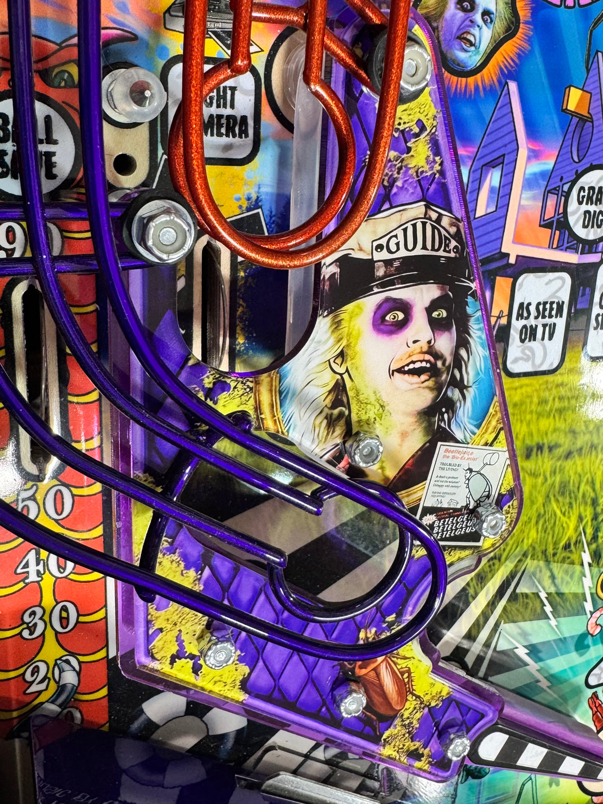 Beetlejuice playfield view showing the installed left slingshot plastic beside purple wireform rails.