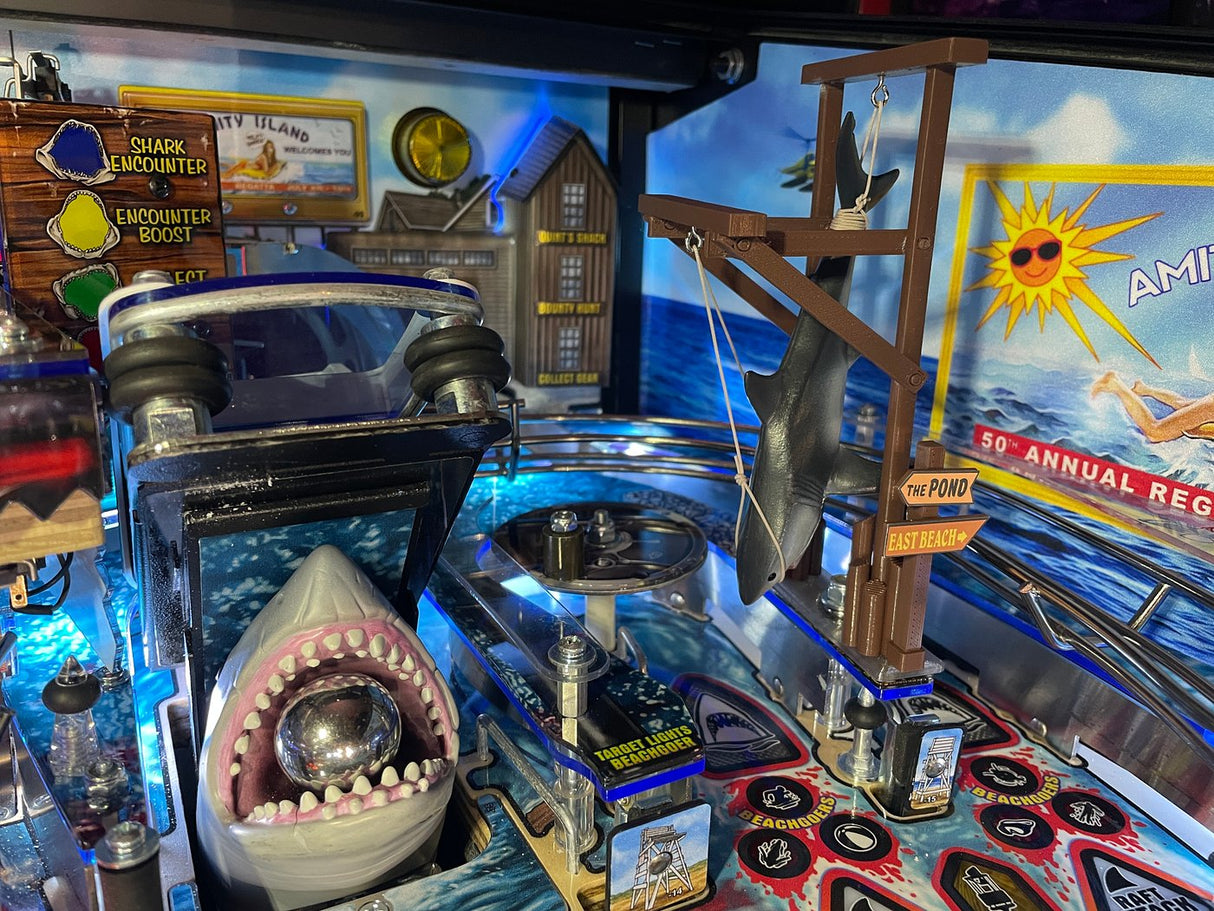 A pinball machine with a clear plastic shark modification resembling the Jaws movie theme, featuring a mouth open with visible teeth.