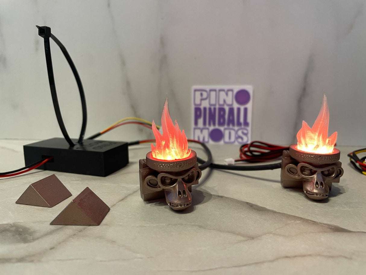 Three King Kong pinball machine mods featuring skull-shaped torches with a flame effect, positioned on a grey surface, with a sign in the background reading 'PINBALL MODS'.