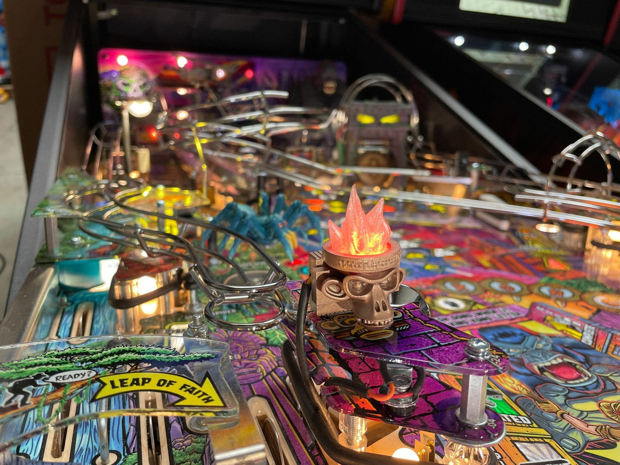 Close-up of a colorful pinball machine with a monkey head torch and vibrant design.