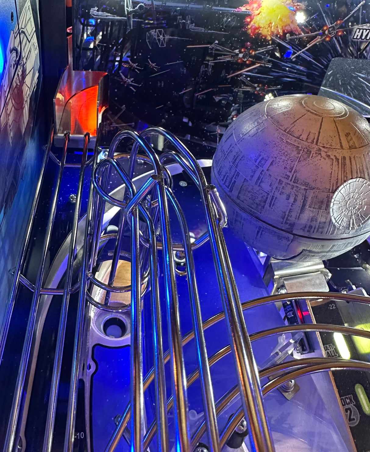 Close-up of a pinball machine with left ramp illlumination, a Death Star figure and metallic rails.