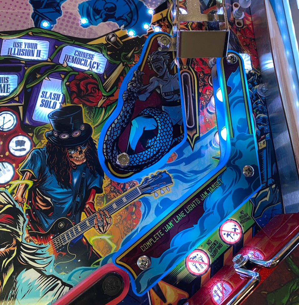 Close-up view of a pinball machine playfield featuring colorful artwork with a musician and a snake, under a clear acrylic protector.