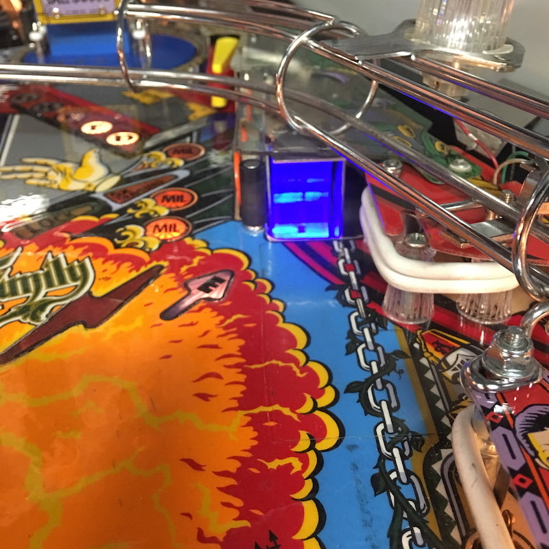 Colorful pinball machine accessory with a glowing blue scoop, attached to a pinball machine's flipper mechanism.