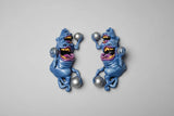 Pair of blue creature sculpts with yellow mouths and purple tongues holding pinballs on a gray background