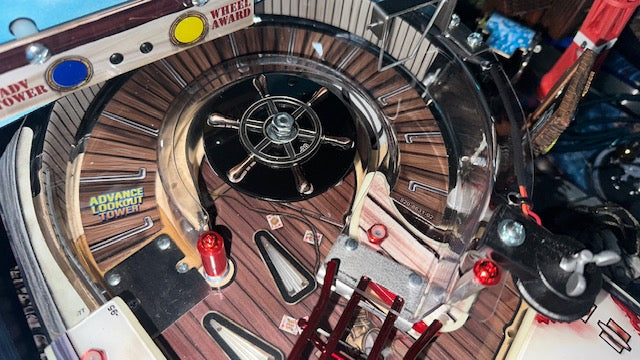 Close-up of a ships wheel on a jaws pinball machine with intricate details and various components.