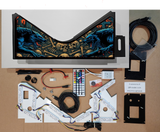 Pinball machine parts and components on a cardboard surface with a detailed artwork backdrop.