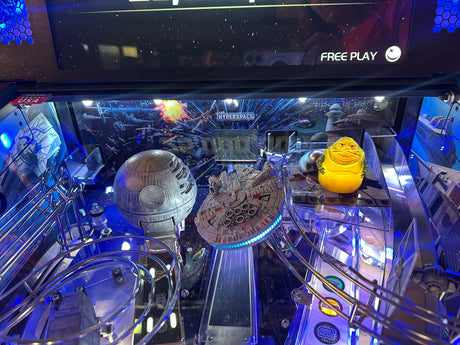 Pinball machine with Star Wars-themed decorations, including a Millennium Falcon and Death Star.