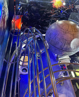Close-up of a pinball machine with left ramp illlumination, a Death Star figure and metallic rails.